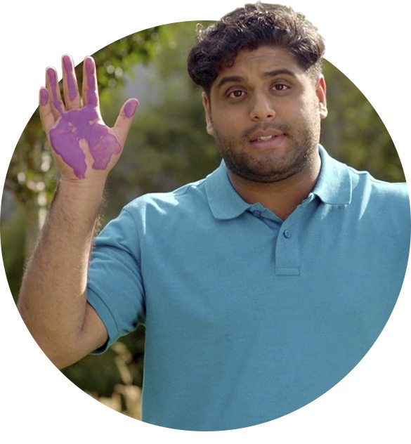 Male playworkers raises his hand towards the camera. There is purple paint on his hand